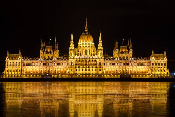 Das beleuchtete Gebäude des ungarischen Parlaments spiegelt sich im Wasser der Donau wider